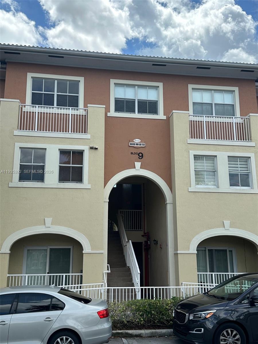 A three-story apartment building exterior features a central arched entryway and white balcony railings — 10800 NW 88th Ter # 213, Doral FL 33178, DORAL, FL