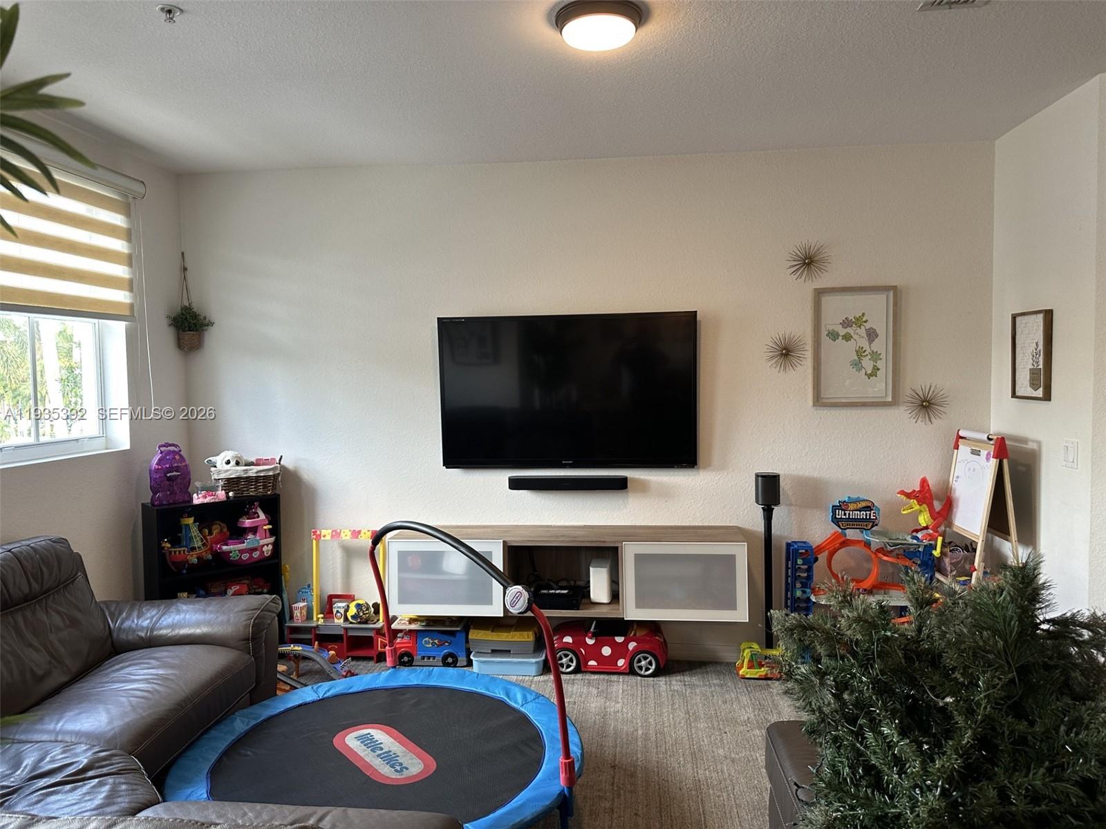 A living room features a wall-mounted television, a media console, and various children's toys — 10800 NW 88th Ter # 213, Doral FL 33178, DORAL, FL
