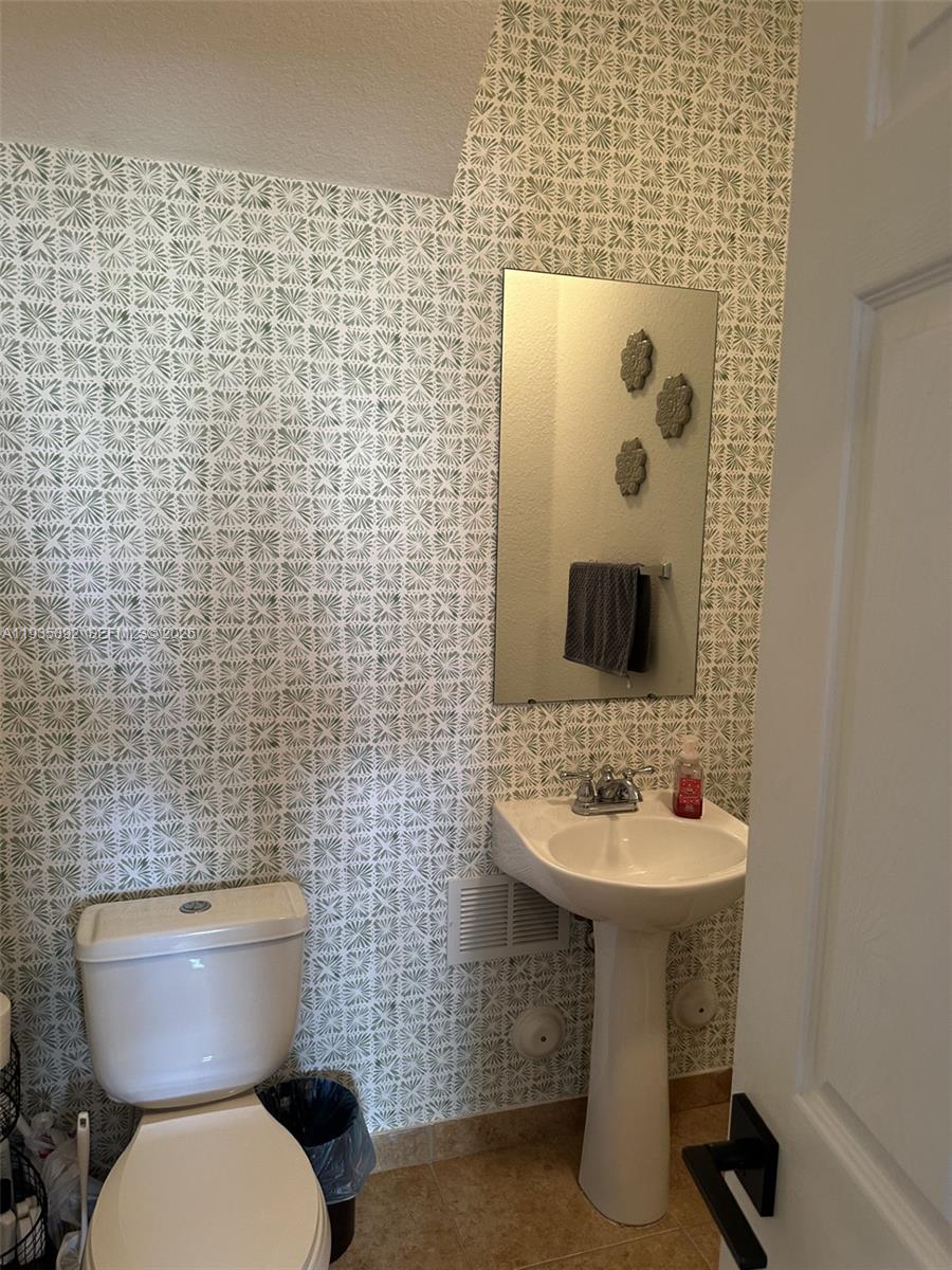 A small bathroom features patterned wallpaper, a pedestal sink, a toilet, and a wall mirror — 10800 NW 88th Ter # 213, Doral FL 33178, DORAL, FL