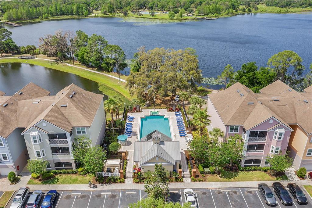 An aerial view shows a community pool situated between two multi-story apartment buildings near a lake — 3446 SOHO ST UNIT 303, ORLANDO, FL