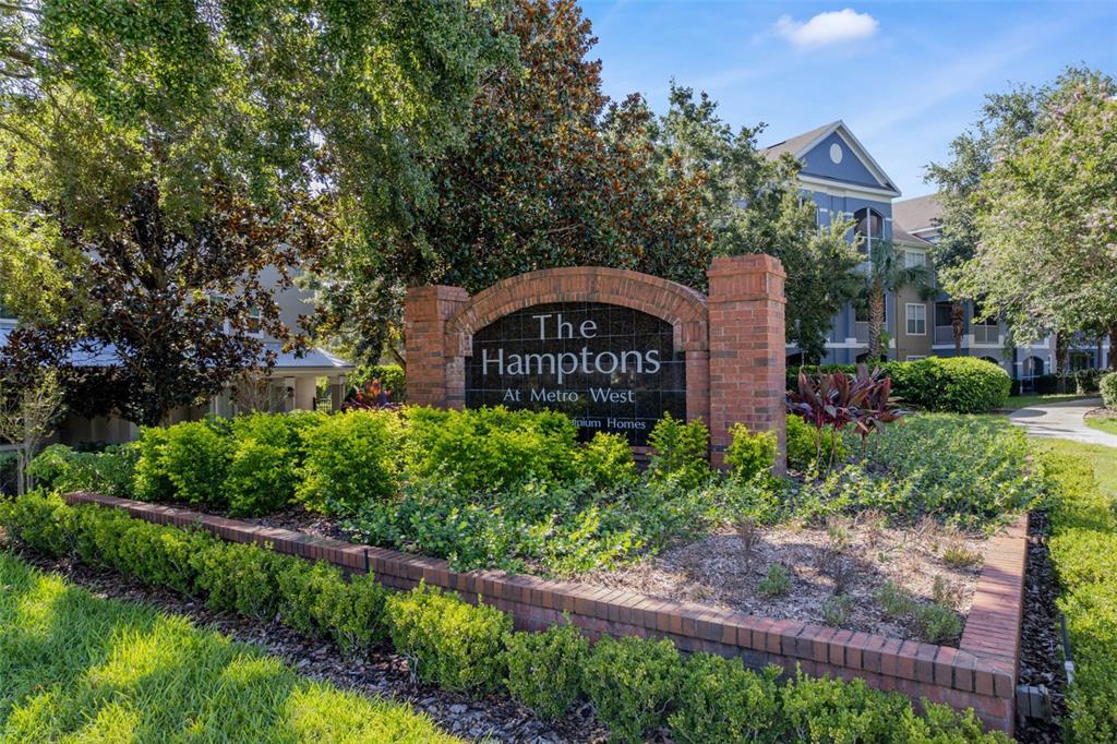 A brick monument sign for The Hamptons at Metro West stands amidst landscaped greenery — 3446 SOHO ST UNIT 303, ORLANDO, FL