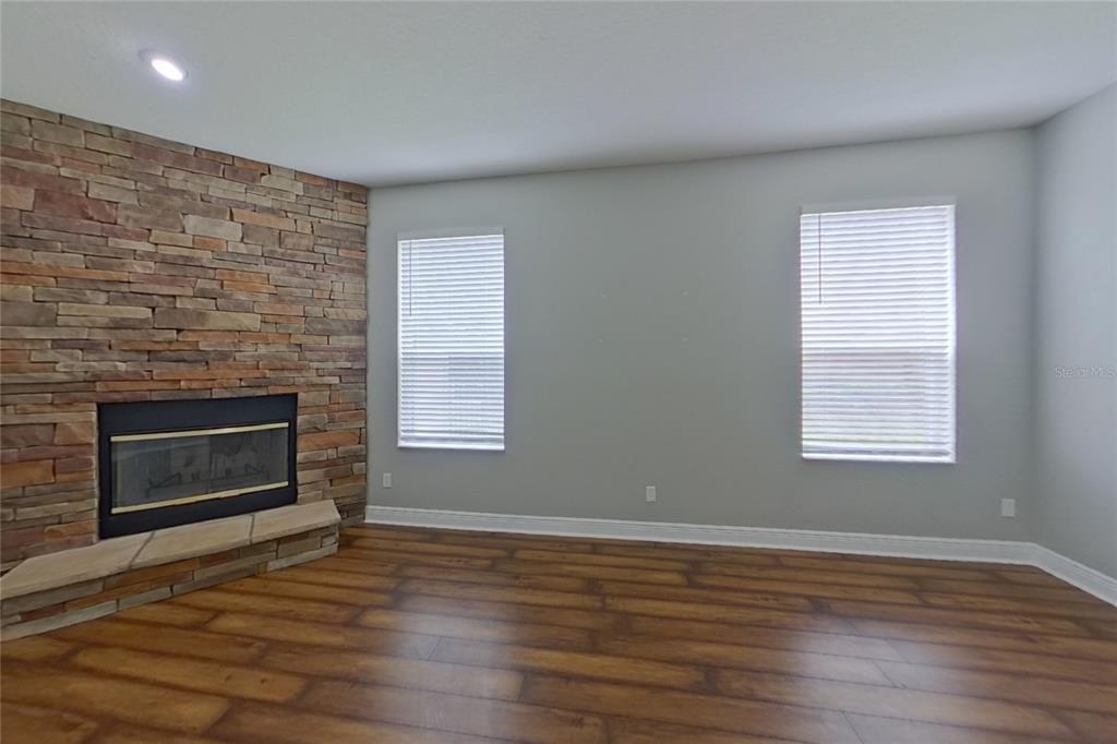A living room with wood-look flooring, a stone corner fireplace, and a ceiling fan — 30136 JUTLAND COURT, MOUNT DORA, FL