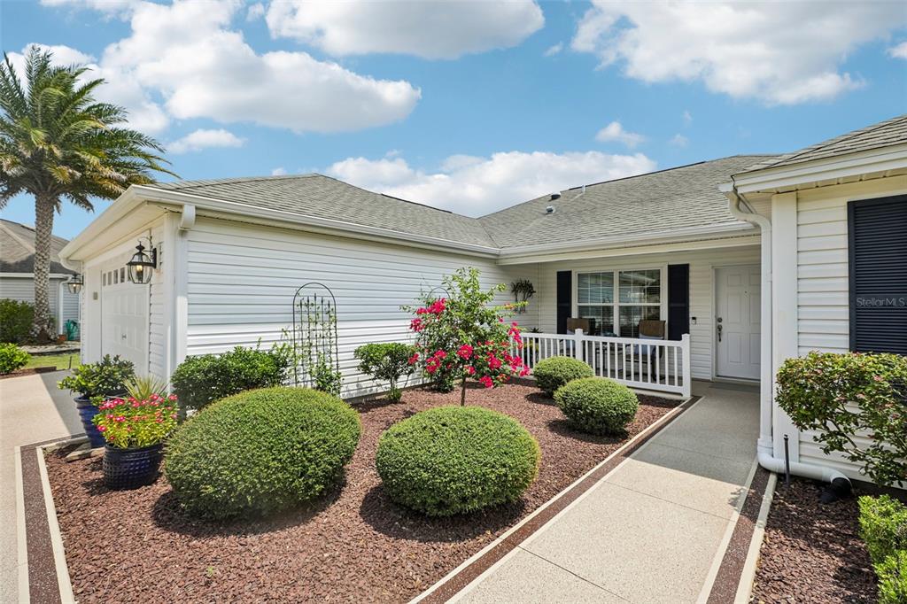 A white house exterior features a landscaped front yard with shrubs and a concrete walkway — 2287 HOPESPRING LOOP, THE VILLAGES, FL