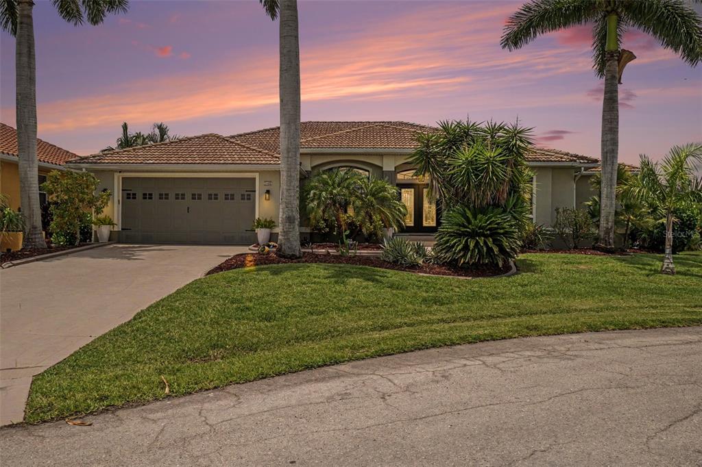 A single-story house with a tile roof, two-car garage, and palm trees at sunset — 1442 KIWI COURT, PUNTA GORDA, FL
