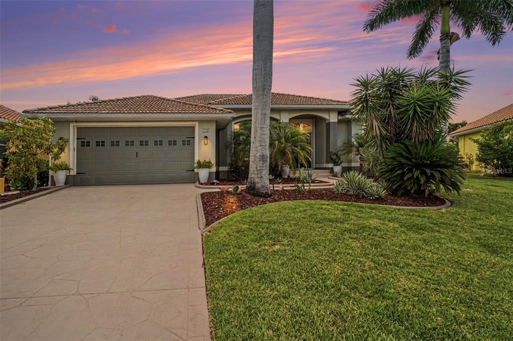A single-story house with a gray garage, tile roof, and landscaped front yard at sunset — 1442 KIWI COURT, PUNTA GORDA, FL