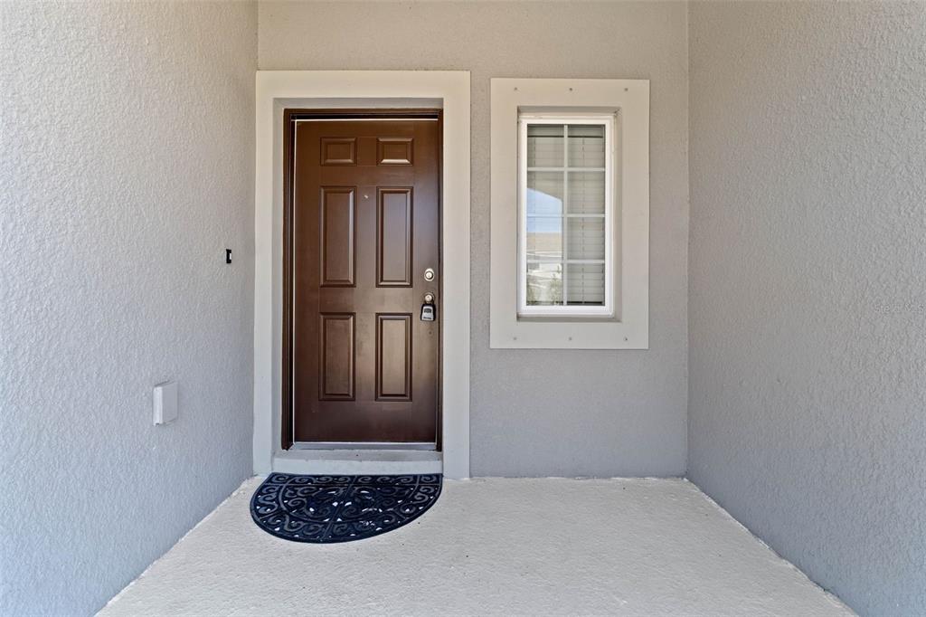 A brown front door and a window are set into a gray stucco exterior wall — 7046 GRAND ELM DRIVE, RIVERVIEW, FL