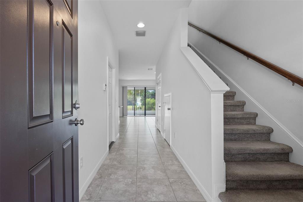 An entryway with tile flooring, a carpeted staircase, and a view toward a rear patio — 7046 GRAND ELM DRIVE, RIVERVIEW, FL