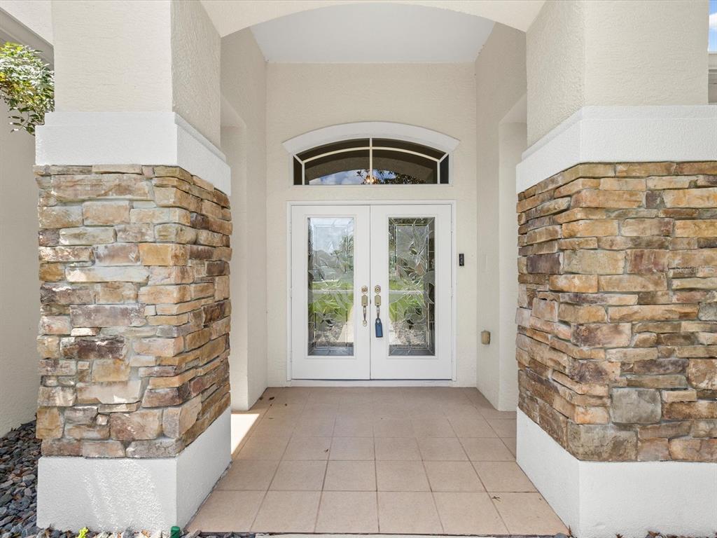 A covered entryway features double glass doors flanked by stone-clad columns and tiled flooring — 4054 INDIAN RIVER STREET, SPRING HILL, FL