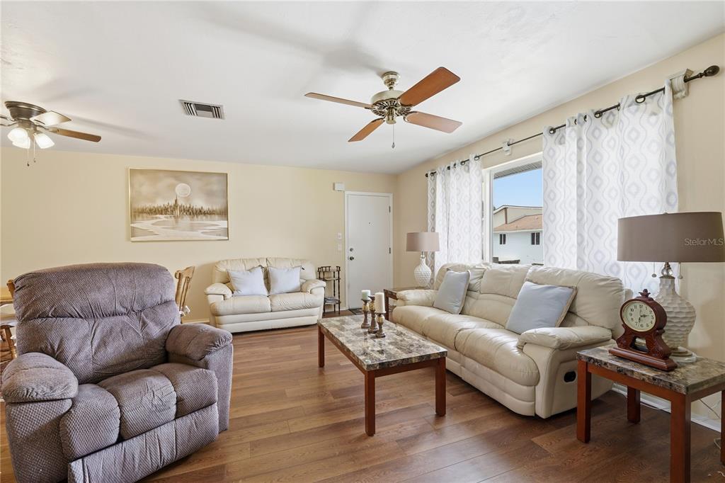 A living room features wood-look flooring, a ceiling fan, and white leather furniture — 22481 WESTCHESTER BOULEVARD UNIT A3, PUNTA GORDA, FL