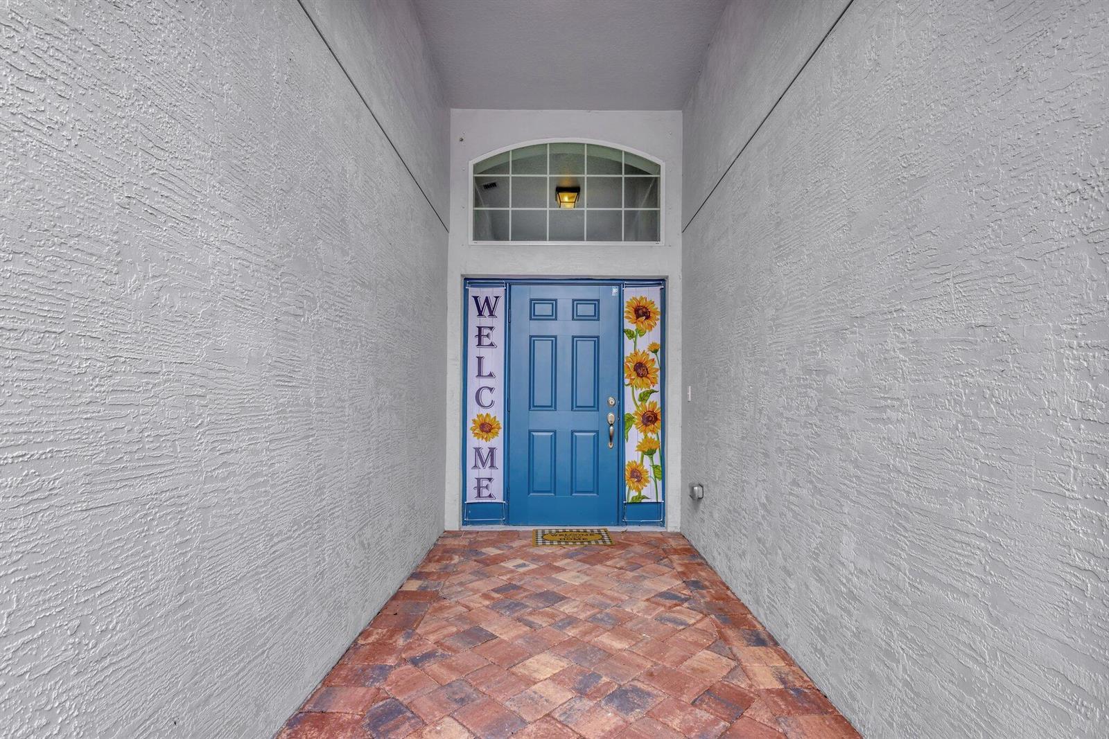 A blue front door with sunflower accents and a welcome sign sits at the entryway — 9709 Starboard Drive, Fort Pierce FL 34945, FORT PIERCE, FL