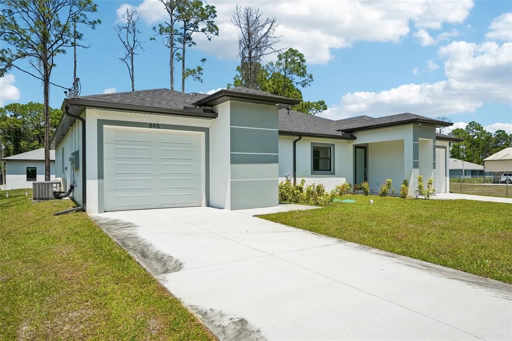 A single-story house with a white exterior, a gray garage door, and a concrete driveway — 845/847 MEADOW ROAD, LEHIGH ACRES, FL