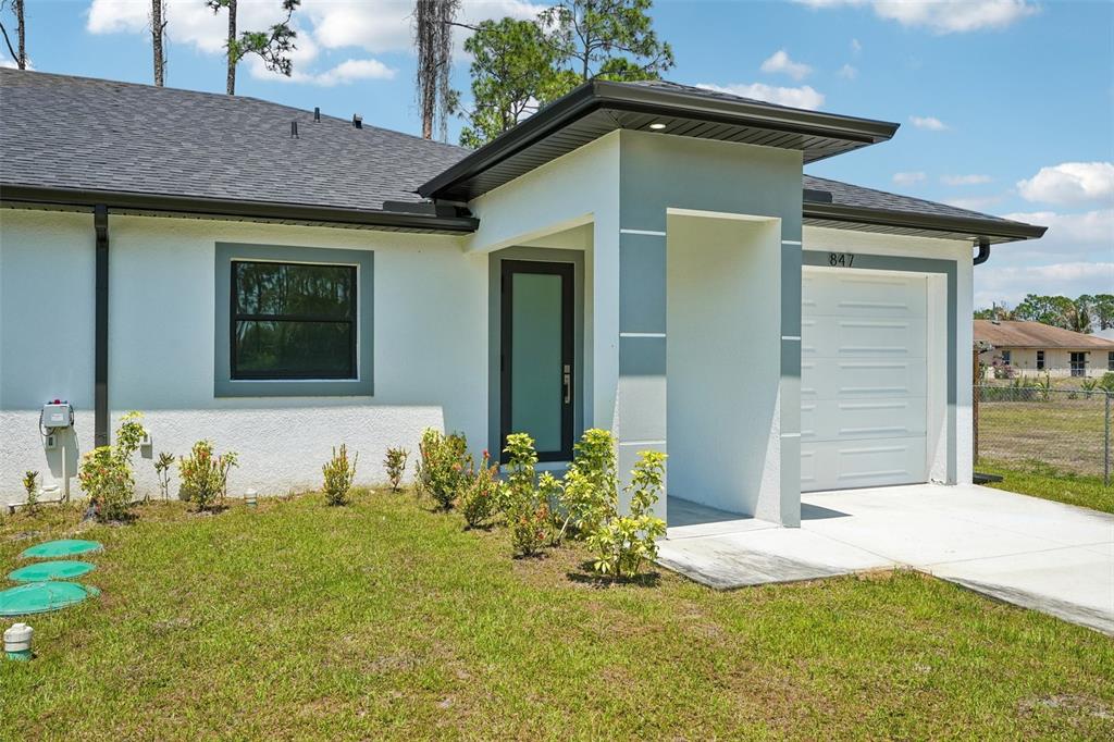 A single-story house with white stucco walls, a gray-trimmed window, and a one-car garage — 845/847 MEADOW ROAD, LEHIGH ACRES, FL