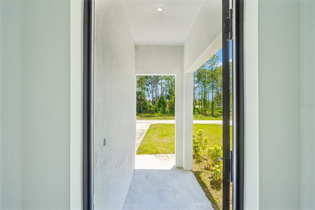 A view from a doorway looking out onto a covered porch and a grassy yard — 845/847 MEADOW ROAD, LEHIGH ACRES, FL