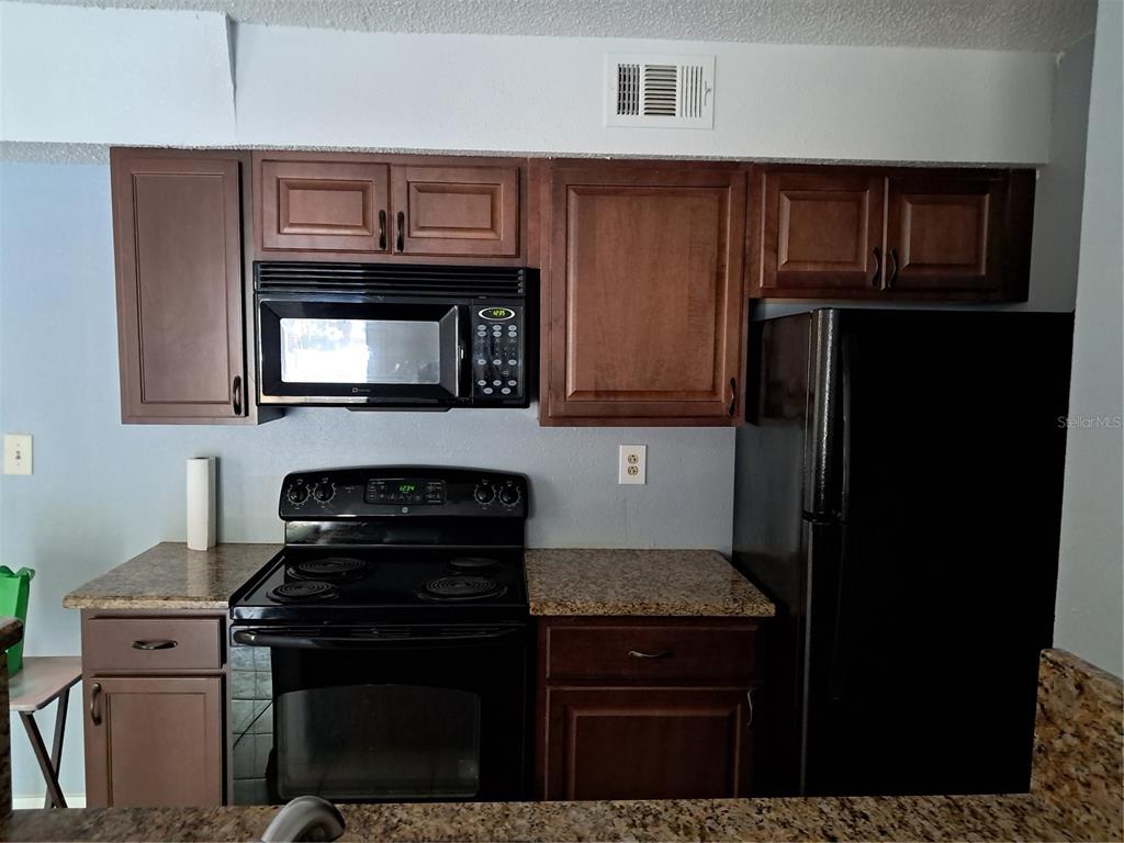 A kitchen features dark wood cabinets, black appliances, and granite countertops — 8648 MALLARD RESERVE DRIVE UNIT 102, TAMPA, FL