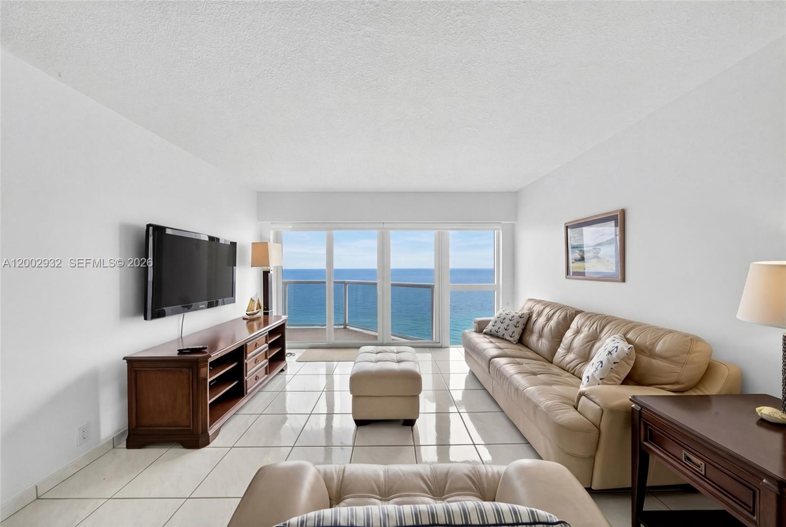 A living room features white tile floors, a tan leather sofa, and a balcony overlooking the ocean — 6767 Collins Ave # 1609, Miami Beach FL 33141, MIAMI BEACH, FL