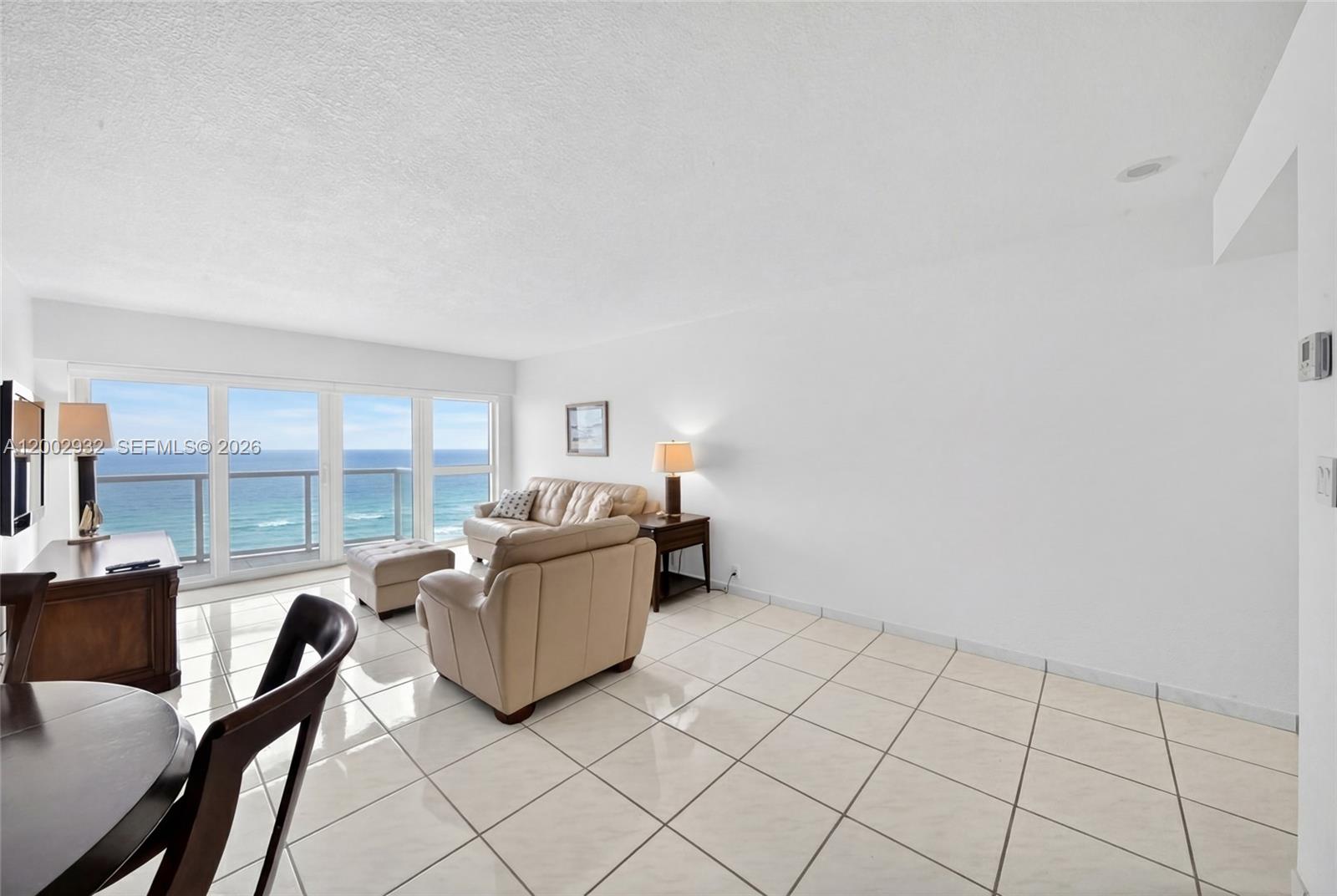 A living room with light tile floors, beige furniture, and a balcony overlooking the ocean — 6767 Collins Ave # 1609, Miami Beach FL 33141, MIAMI BEACH, FL