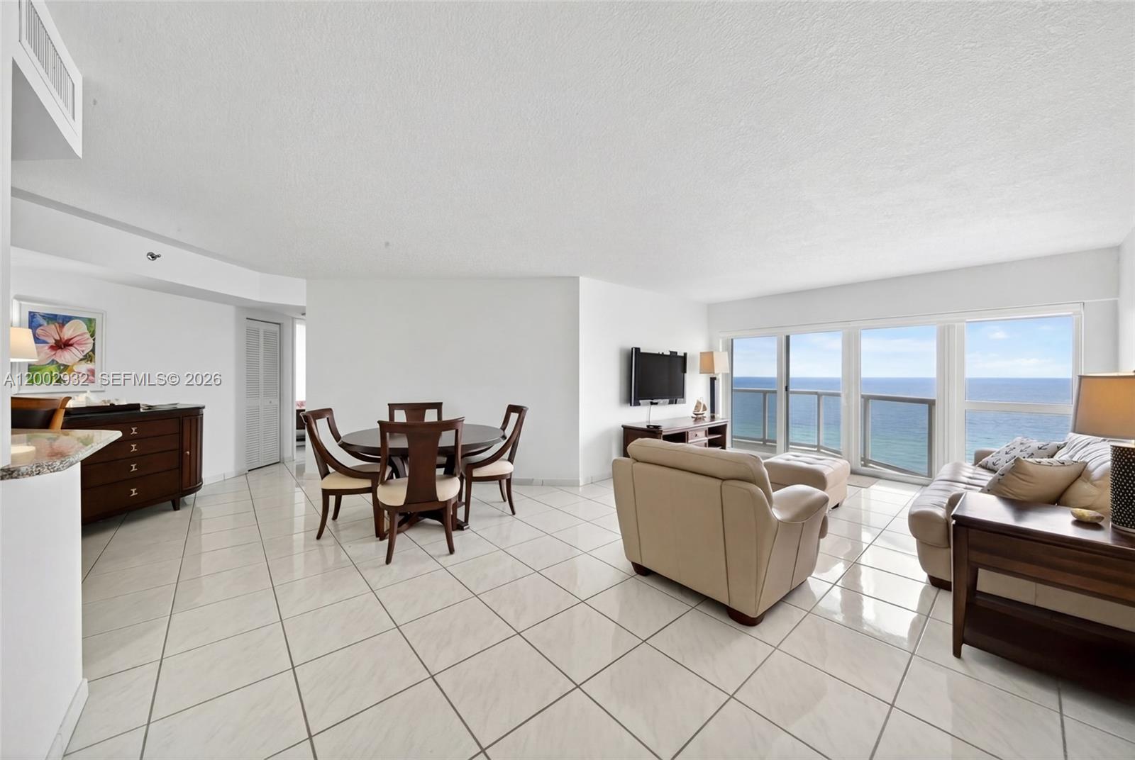 An open-concept living and dining area features white tile floors and floor-to-ceiling ocean views — 6767 Collins Ave # 1609, Miami Beach FL 33141, MIAMI BEACH, FL