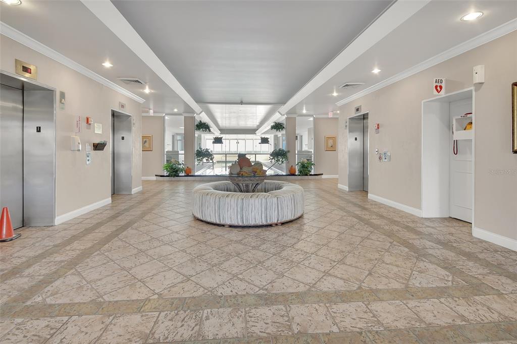 A lobby features a circular ottoman, tiled floors, two elevators, and a view of a pool — 2937 S ATLANTIC AVENUE UNIT 2009, DAYTONA BEACH SHORES, FL