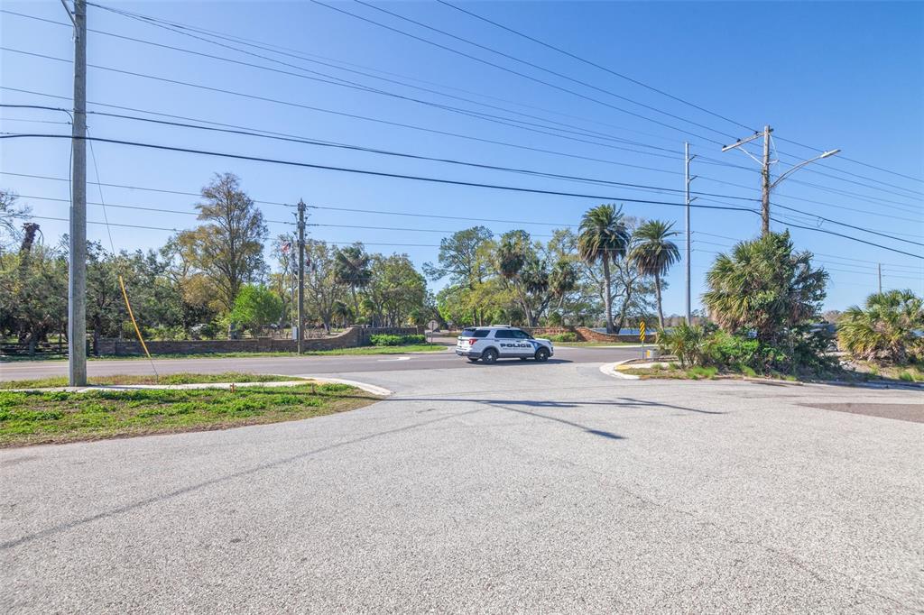 A police vehicle drives past a park entrance with palm trees and utility poles — 1200 8TH AVENUE SW UNIT 1, LARGO, FL