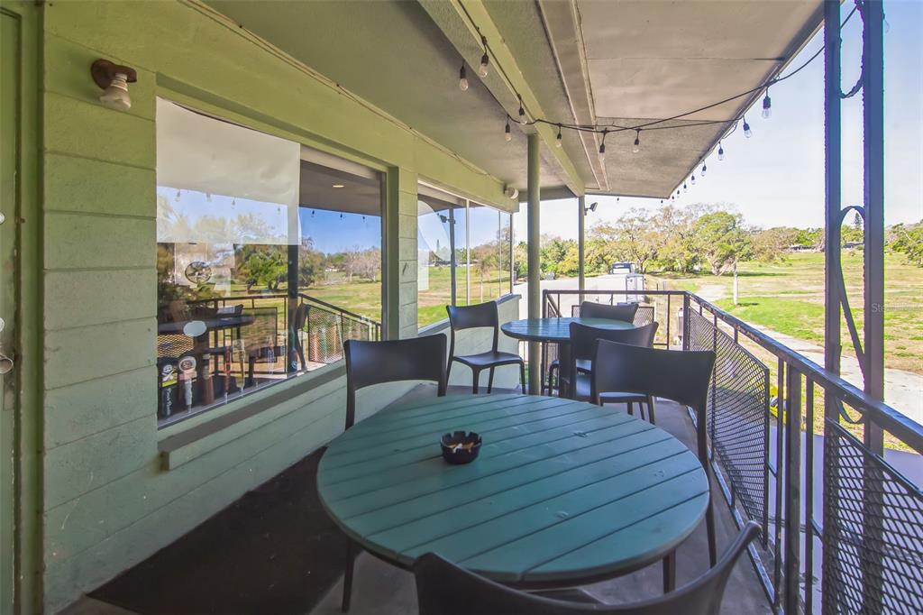A covered outdoor balcony features a round green table, chairs, and string lights overlooking grass — 1200 8TH AVENUE SW UNIT 1, LARGO, FL