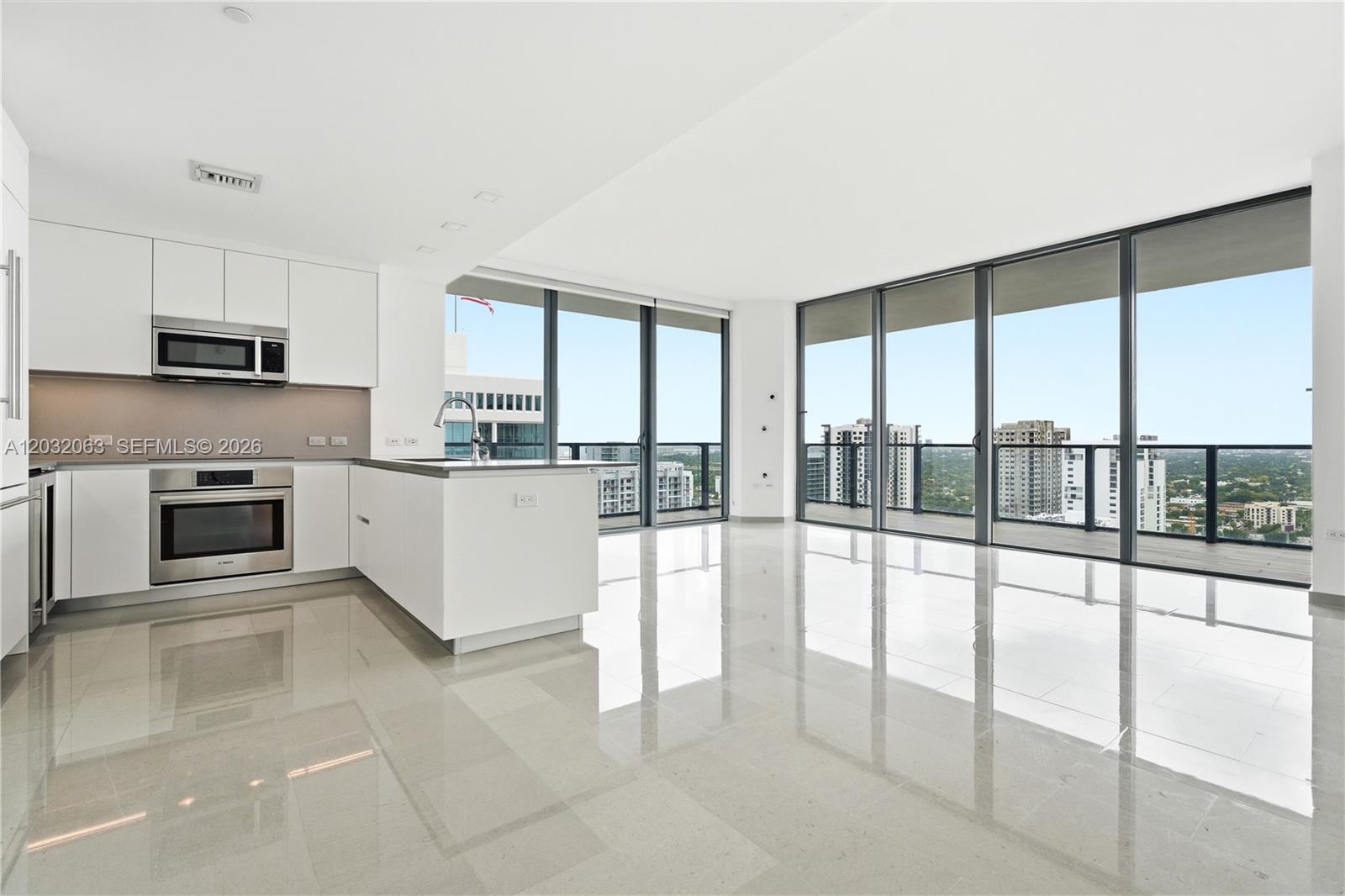 A modern kitchen with white cabinets and stainless steel appliances opens to a bright living area — 88 SW 7th St # 2302, Miami FL 33130, MIAMI, FL
