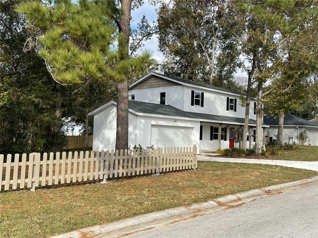 A two-story house with white siding, a garage, and a wooden picket fence in front — 849 LAURELRIDGE COURT, BROOKSVILLE, FL