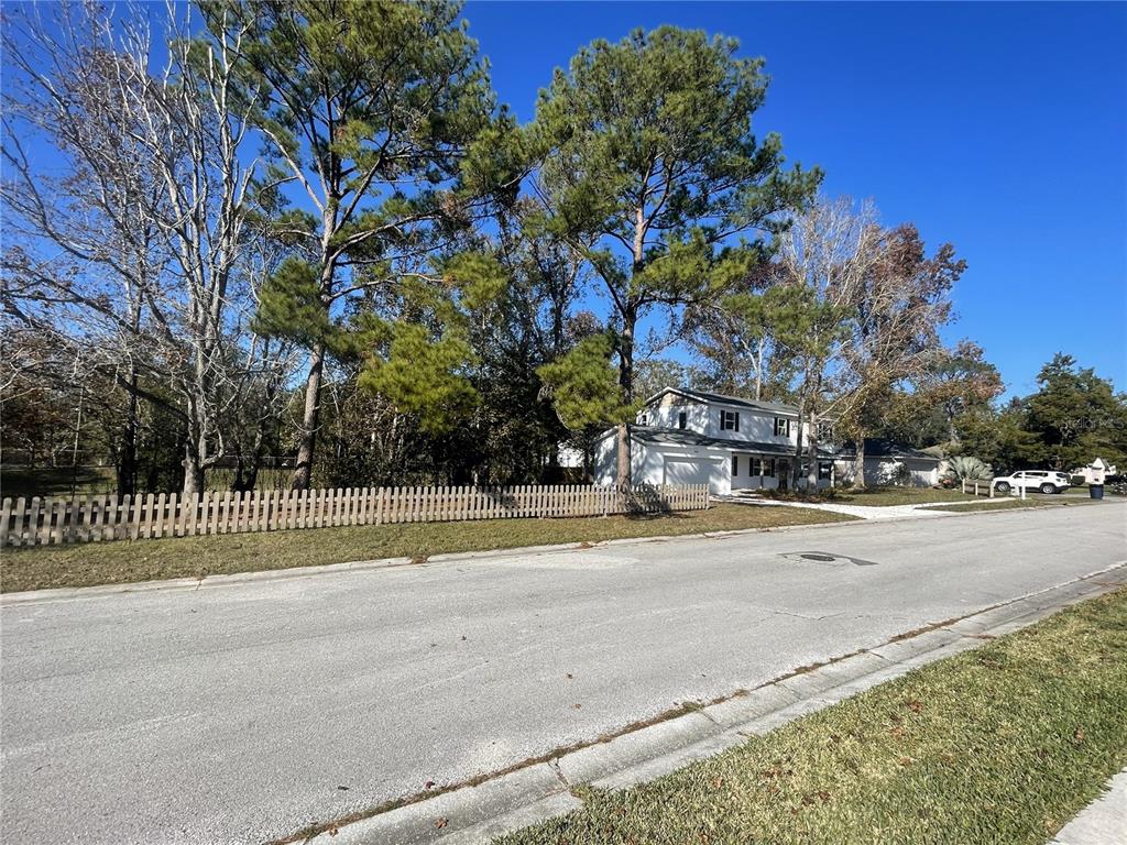 A two-story house sits behind a wooden fence next to a street and trees — 849 LAURELRIDGE COURT, BROOKSVILLE, FL