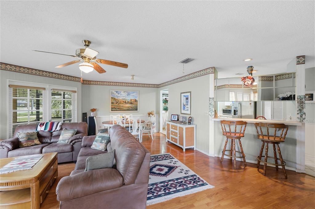 A living room and dining area with hardwood floors, a ceiling fan, and bar seating — 4336 CACTUS AVENUE, SARASOTA, FL