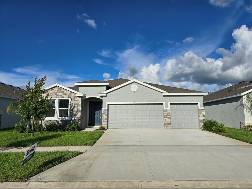 A single-story house with a gray stucco exterior, stone accents, and a three-car garage — 33965 FIELD MAPLE LOOP, WESLEY CHAPEL, FL