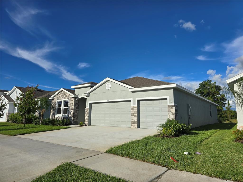 A single-story house with a gray stucco exterior, stone accents, and a three-car garage — 33965 FIELD MAPLE LOOP, WESLEY CHAPEL, FL