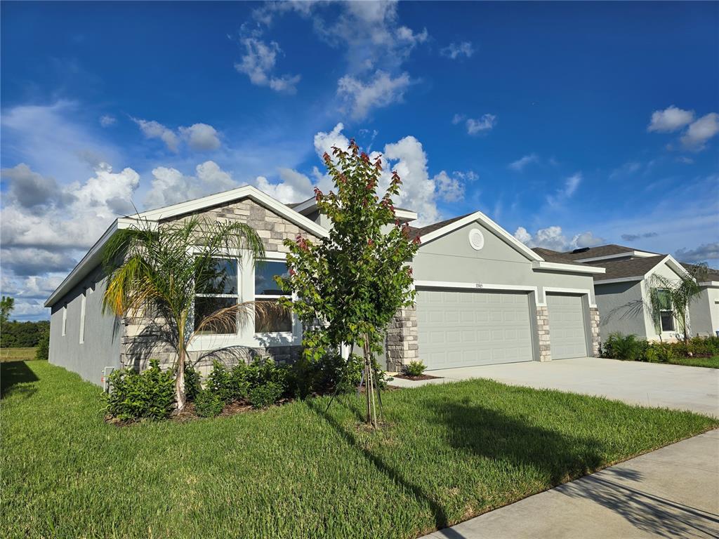 A single-story house with a stone facade, a three-car garage, and a green lawn — 33965 FIELD MAPLE LOOP, WESLEY CHAPEL, FL