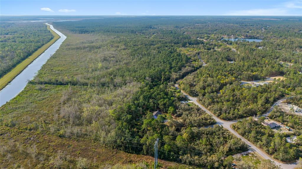 An aerial view shows a house surrounded by dense forest next to a long canal — 475 FISHER ROAD, OCKLAWAHA, FL