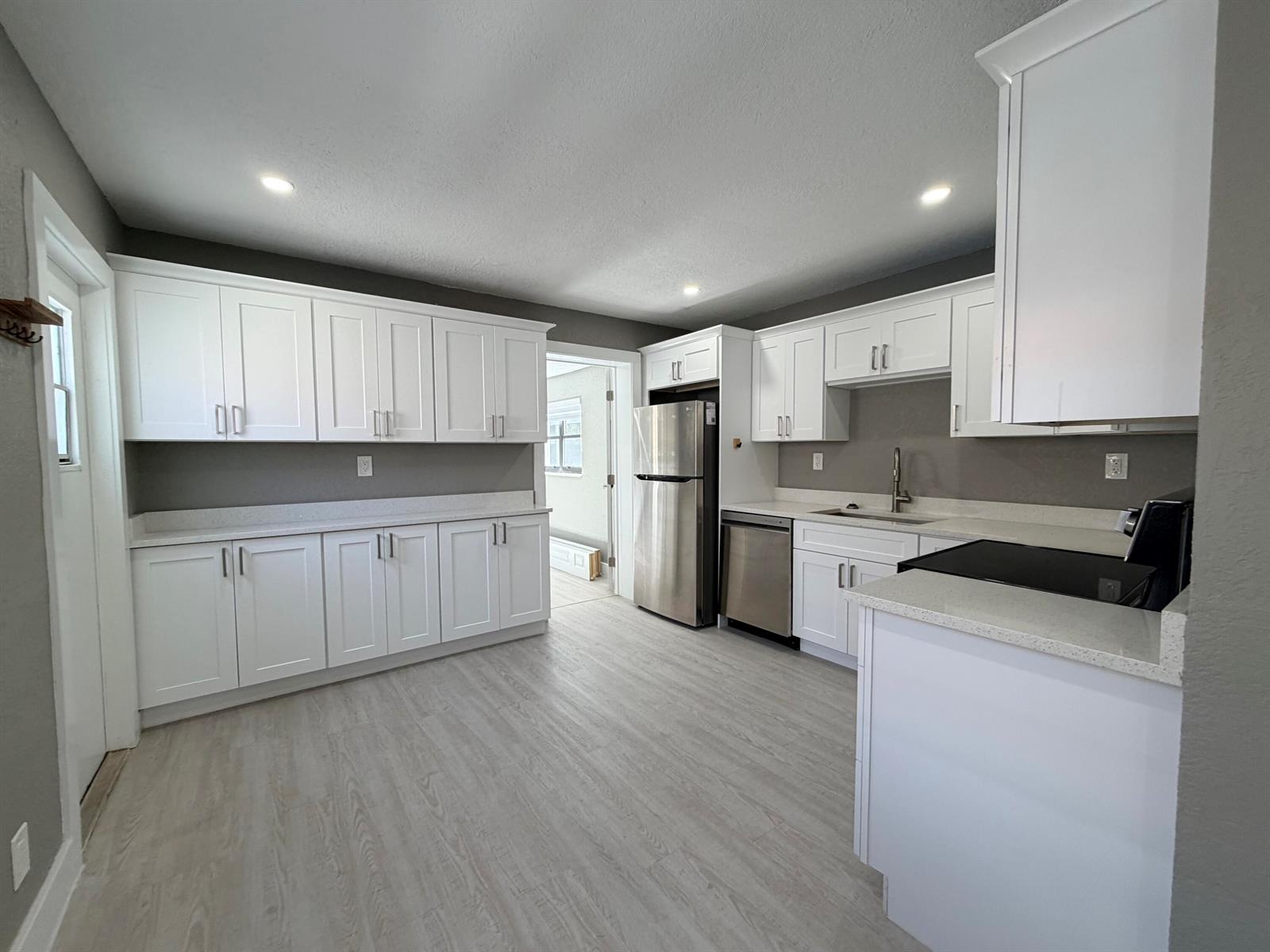 A kitchen features white cabinets, stainless steel appliances, gray walls, and light wood-look flooring — 827 Franklin Road, West Palm Beach FL 33405, WEST PALM BEACH, FL