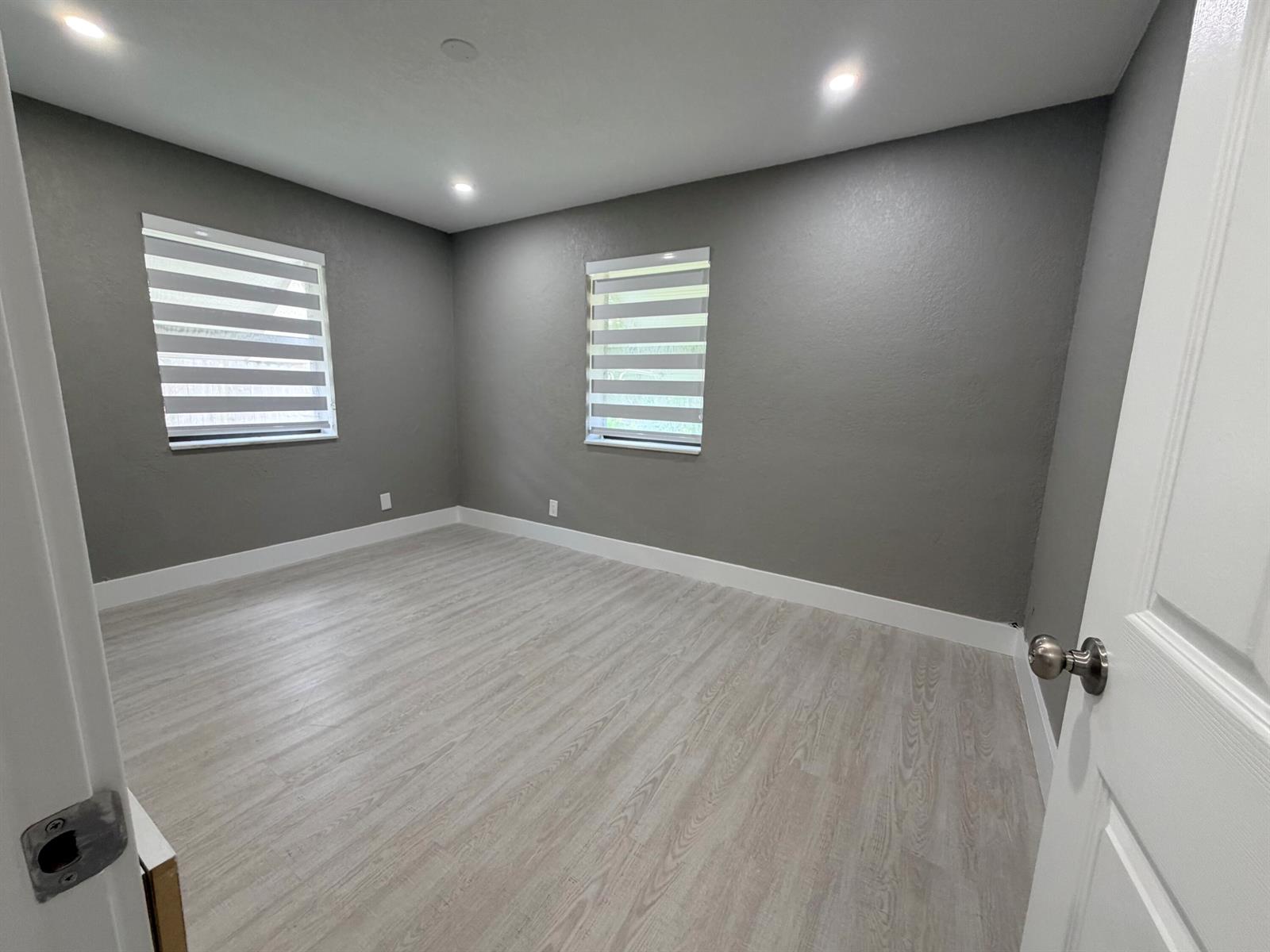 An empty bedroom features gray walls, light wood-look flooring, and two windows with zebra blinds — 827 Franklin Road, West Palm Beach FL 33405, WEST PALM BEACH, FL