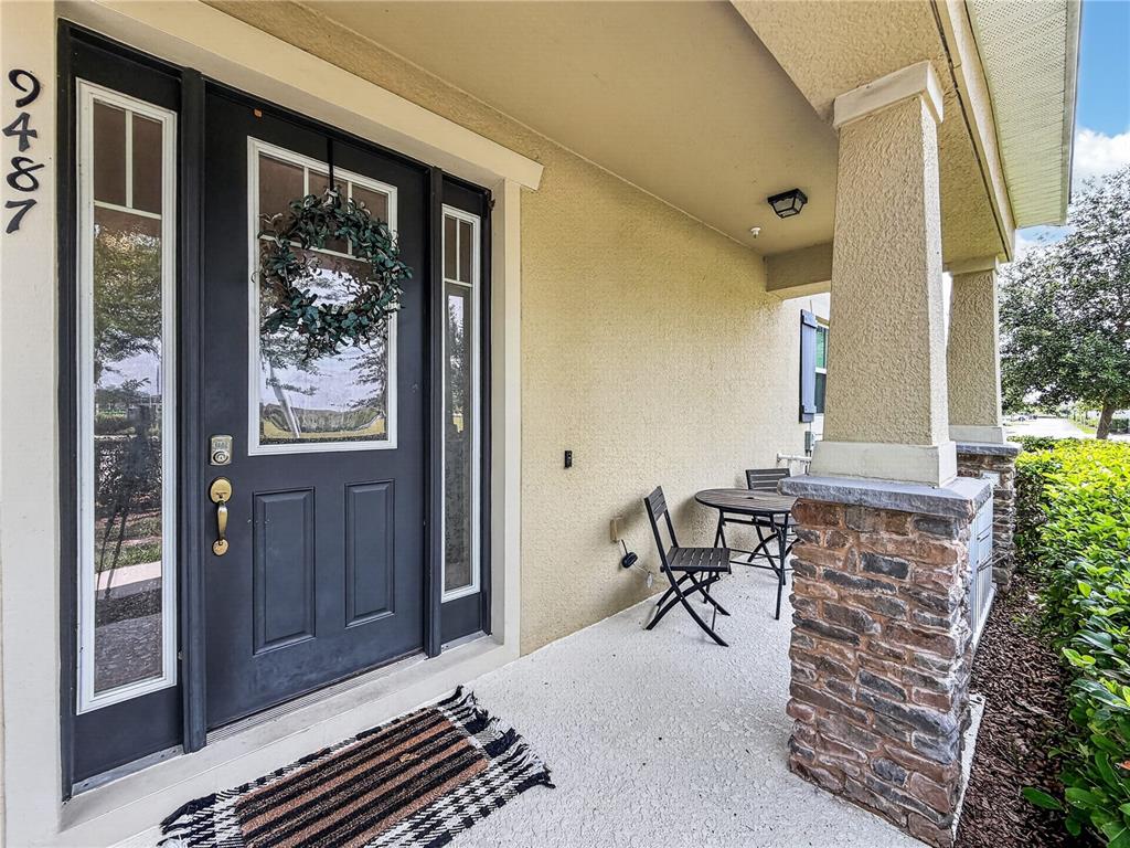 A covered front porch features a dark door, a small table with chairs, and stone columns — 9487 RANDAL PARK BOULEVARD, ORLANDO, FL
