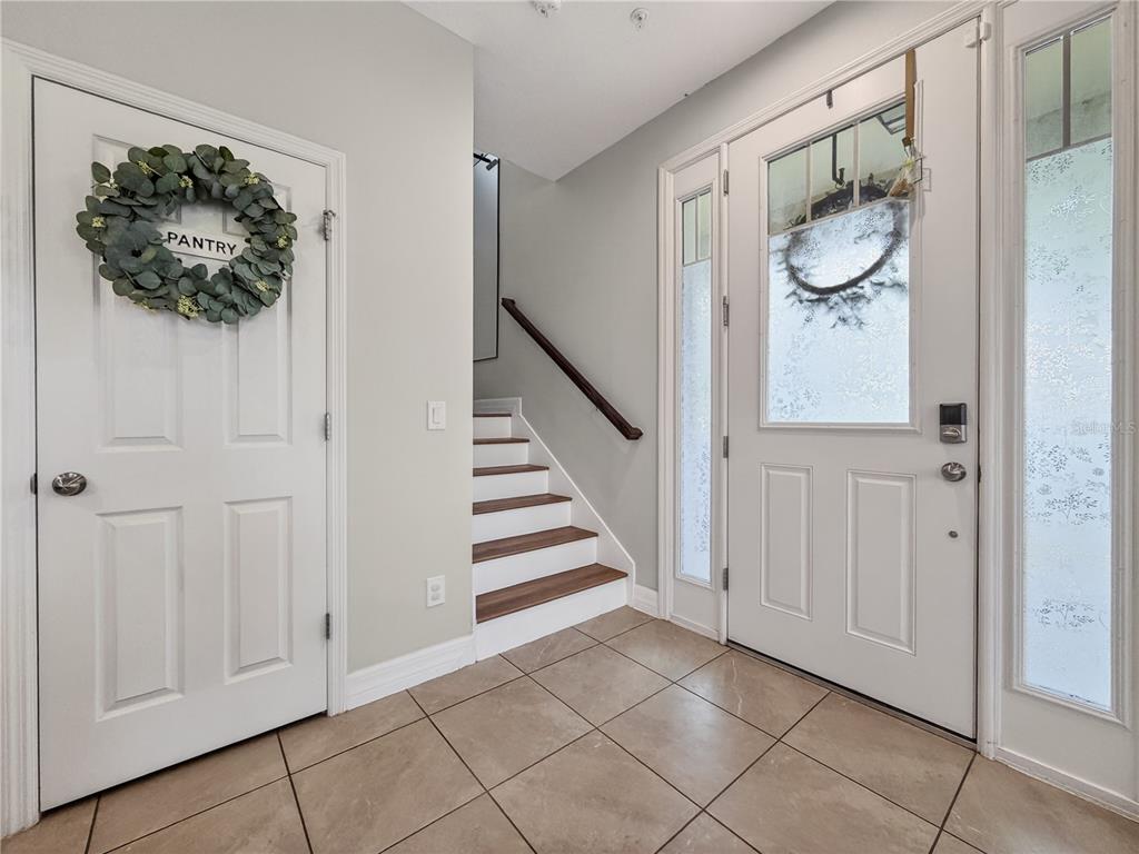 A tiled entryway features a staircase, a pantry door with a wreath, and a front door — 9487 RANDAL PARK BOULEVARD, ORLANDO, FL