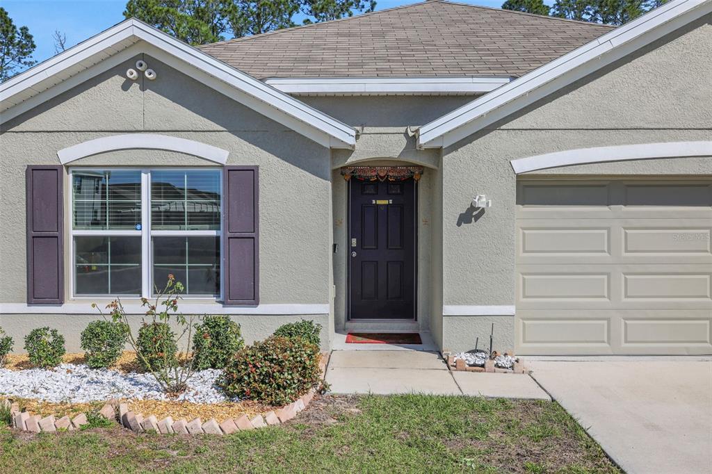 The exterior of a single-story house features a tan stucco facade, a garage, and landscaping — 8640 SW 49TH CIRCLE, OCALA, FL