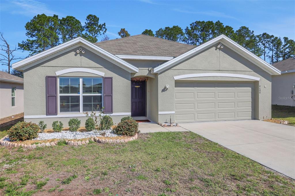A single-story house with a beige stucco exterior, a two-car garage, and a front lawn — 8640 SW 49TH CIRCLE, OCALA, FL