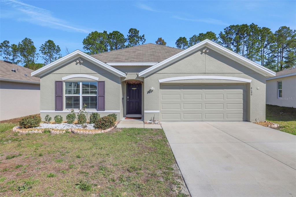 A single-story house with a beige stucco exterior, a two-car garage, and a front lawn — 8640 SW 49TH CIRCLE, OCALA, FL