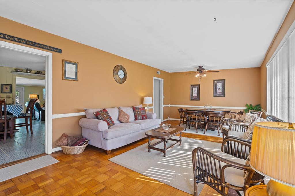 A living room with tan walls, a light gray sofa, wooden floors, and a dining area — 3808 SAN GABRIEL DRIVE, PENSACOLA, FL