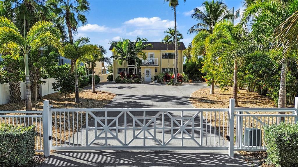 A two-story yellow building with a balcony and palm trees sits near a paved path — 19936 GULF BOULEVARD, INDIAN SHORES, FL