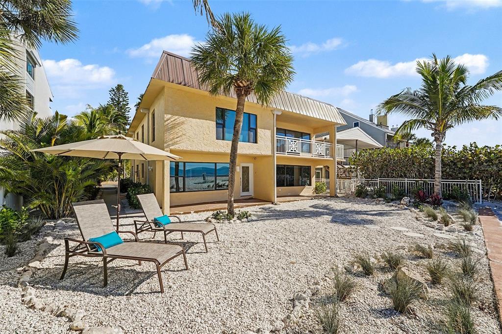 A two-story yellow house with a gravel yard, palm trees, and two lounge chairs — 19936 GULF BOULEVARD, INDIAN SHORES, FL