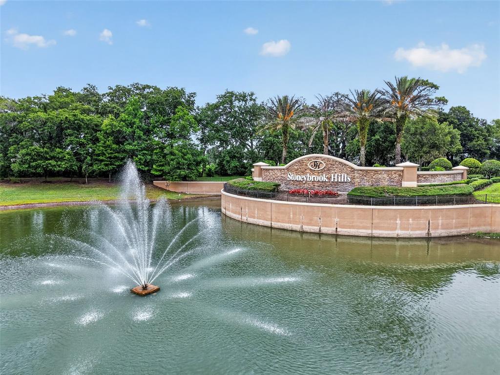 A fountain sprays water in a pond in front of a Stoneybrook Hills entrance sign — 5828 PUZO PLACE, MOUNT DORA, FL