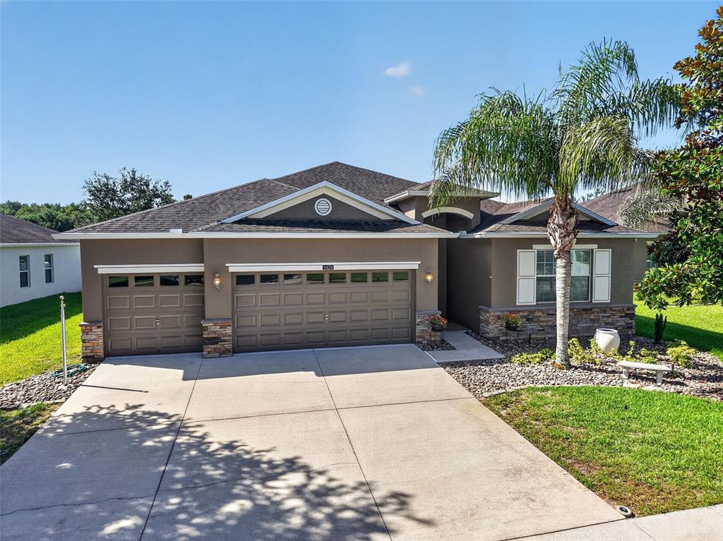 A single-story house with a three-car garage, stone accents, and a palm tree in front — 5828 PUZO PLACE, MOUNT DORA, FL
