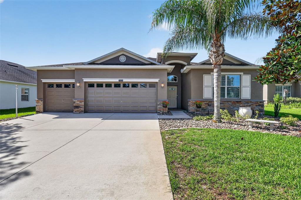 A single-story suburban house with a three-car garage, stone accents, and a palm tree — 5828 PUZO PLACE, MOUNT DORA, FL