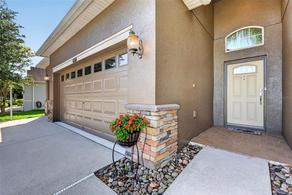 A tan house exterior features a garage, a front door, and a stone-accented pillar — 5828 PUZO PLACE, MOUNT DORA, FL