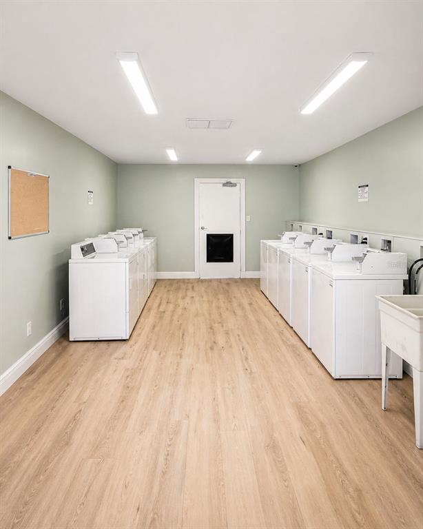 A laundry room with light green walls, wood-look flooring, and multiple white washing machines — 1179-1179 BENTLEY ROAD UNIT 1, LEESBURG, FL
