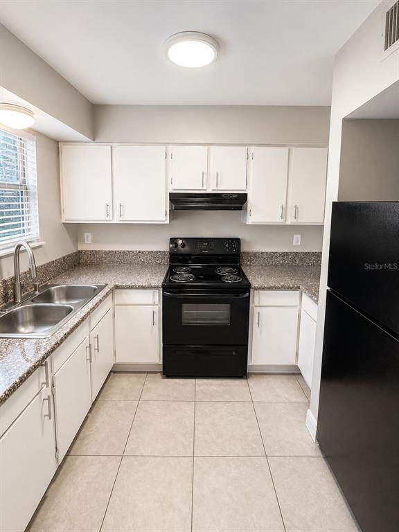 A kitchen features white cabinets, black appliances, granite countertops, and light-colored tile flooring — 1179-1179 BENTLEY ROAD UNIT 1, LEESBURG, FL