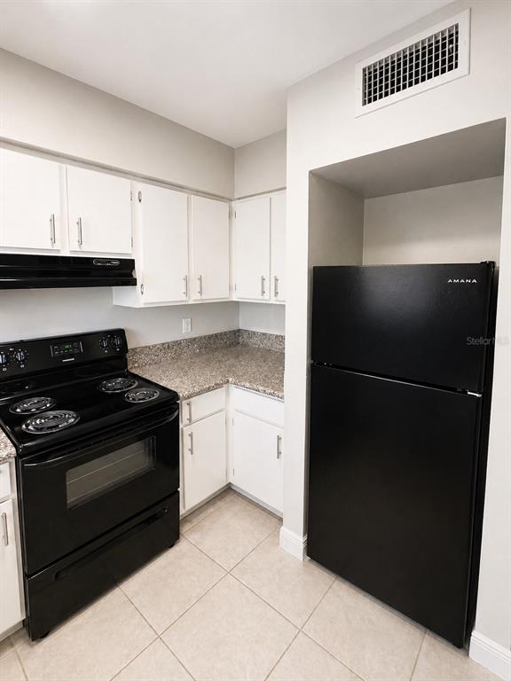 A kitchen features white cabinets, granite countertops, black appliances, and light-colored tile flooring — 1179-1179 BENTLEY ROAD UNIT 1, LEESBURG, FL