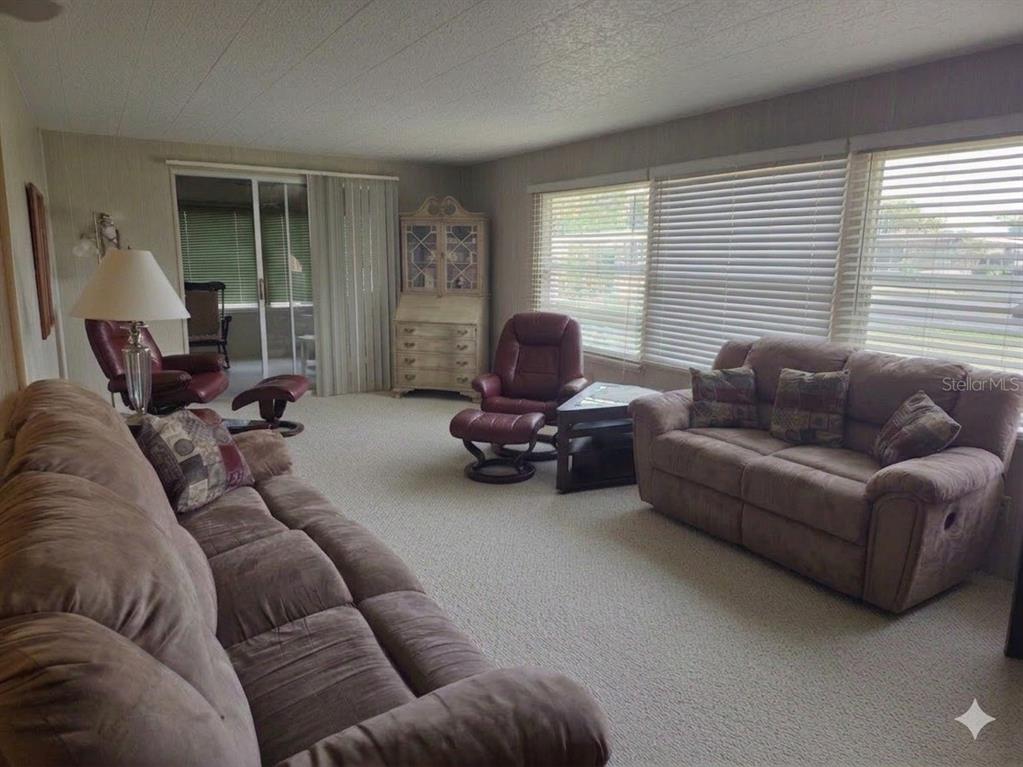 A living room features beige carpeting, a brown sofa, two recliners, and large window blinds — 9900 ULMERTON ROAD UNIT 13, LARGO, FL